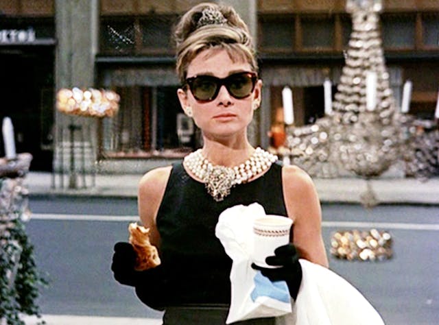 Audrey Hepburn in Breakfast at Tiffany's eating a croissant and drinking coffee.